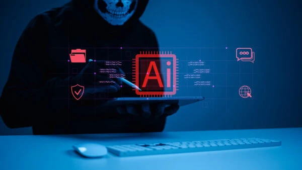 A person in a dark hoodie and skull mask uses a tablet, with a digital AI chip graphic and cybersecurity icons overlaid in a blue-lit setting.