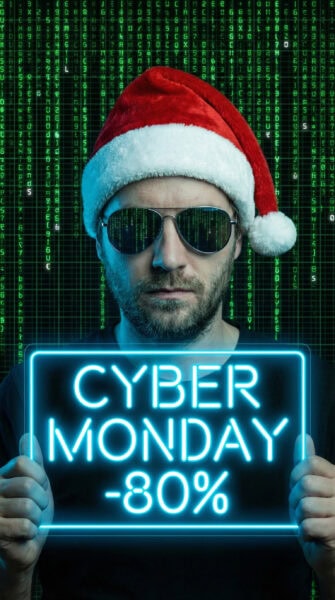 Man in Santa hat and sunglasses holds neon sign reading "Cyber Monday -80%" against digital matrix background.