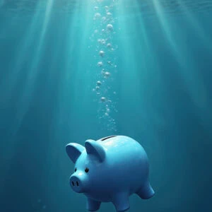A blue piggy bank is submerged underwater with bubbles rising and sunlight streaming down from above.