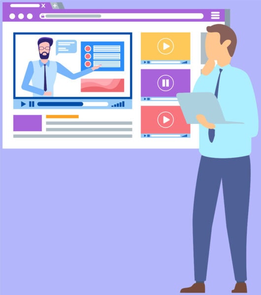 A person holding a laptop stands in front of a large computer screen displaying an online video lecture with a presenter and media thumbnails.