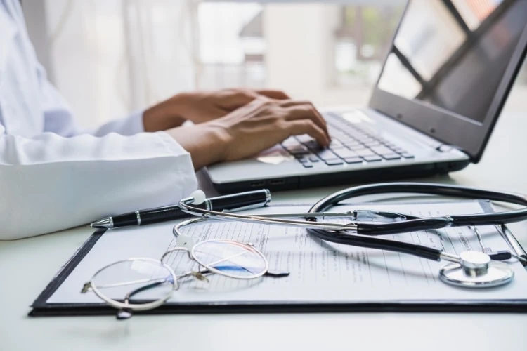 A doctor is typing on a laptop in a healthcare organization.