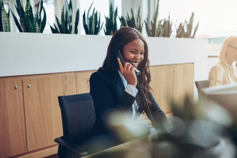 Professional woman laughing during a phone conversation in an office setting, representing Telecommunications services.